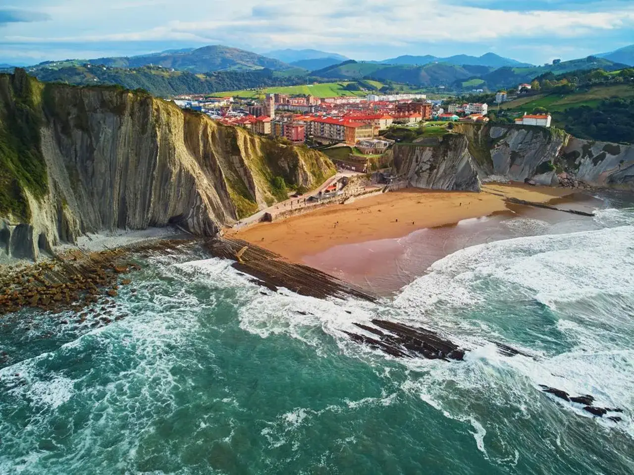 Vista aérea de la playa de Ondarroa, San Sebastián, con acantilados imponentes y el mar Cantábrico rompiendo en la costa.