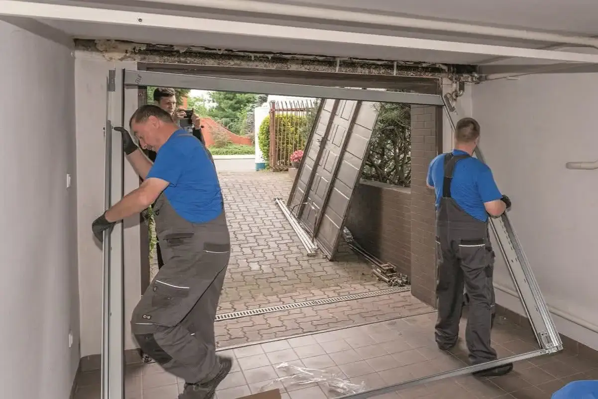 Montaż bramy garażowej uchylnej w toku. Dw&oacute;ch fachowc&oacute;w pracuje nad instalacją, jeden przy framudze, drugi z elementem bramy.