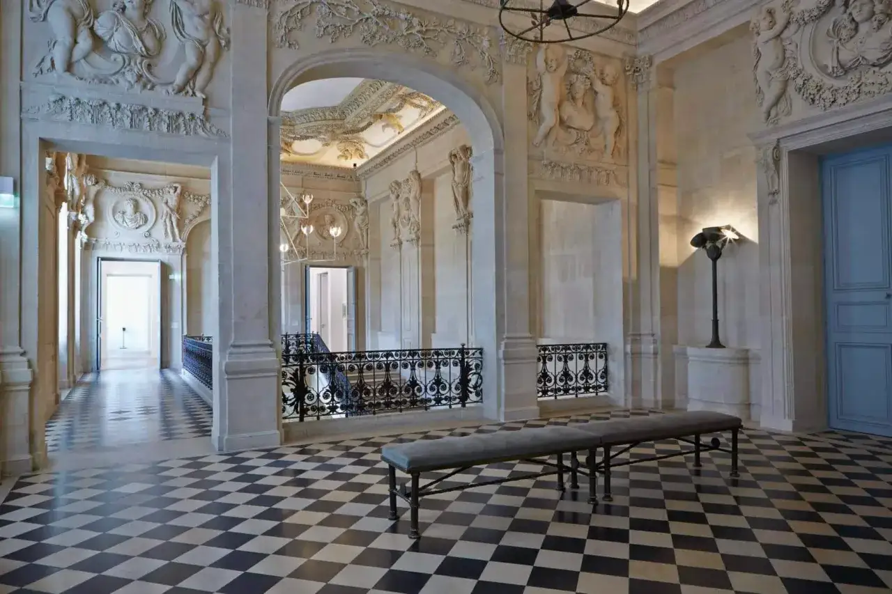 Elegancki hol w muzeum Picassa w Paryżu. Kamienne rzeźby, czarno-biała szachownica na podłodze i stylowa ławka tworzą atmosferę.