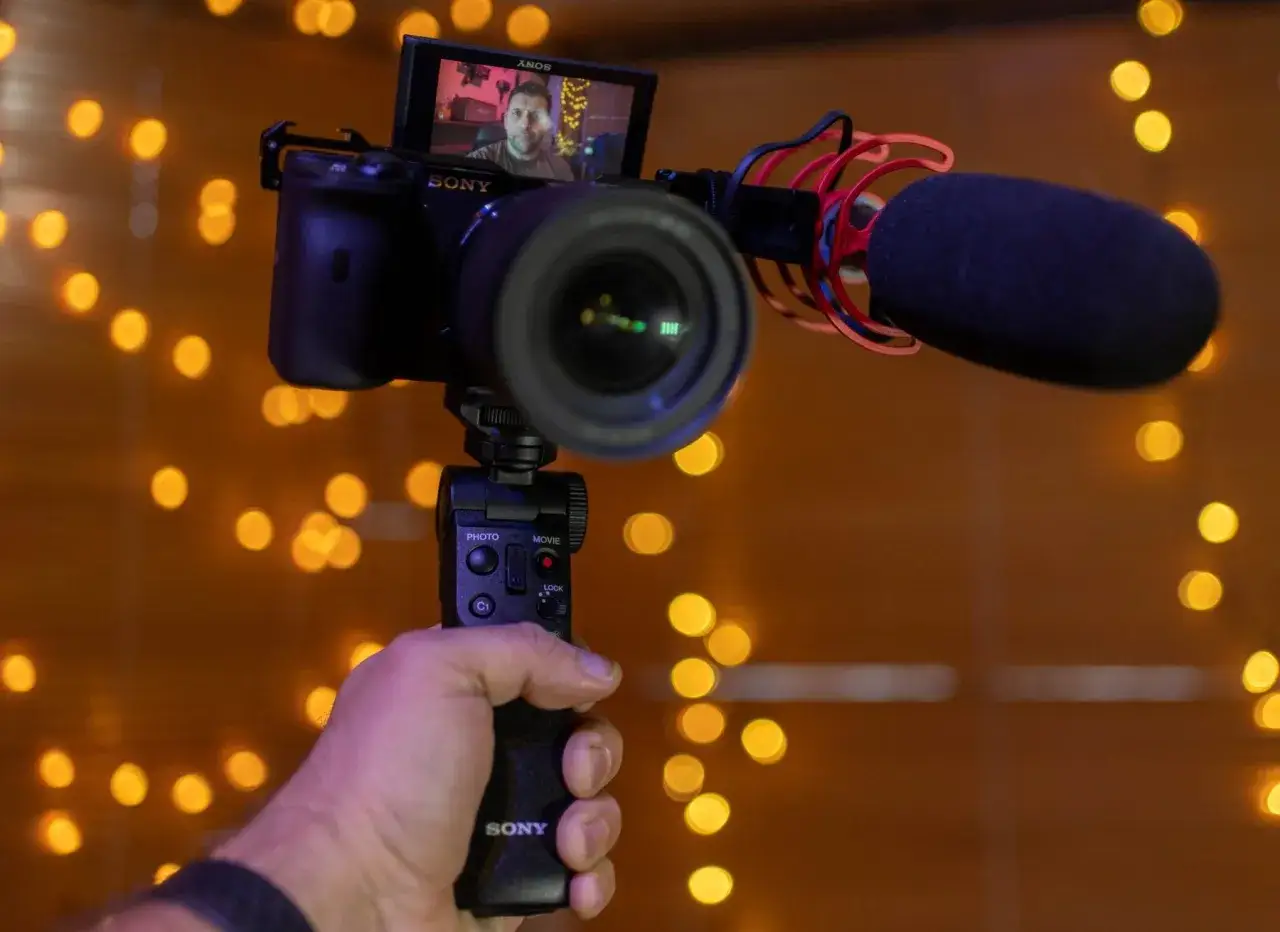 Ręka trzyma aparat Sony z mikrofonem, gotowy do nagrania. To sprzęt do tworzenia materiałów, czyli do tego, co to jest vlog.