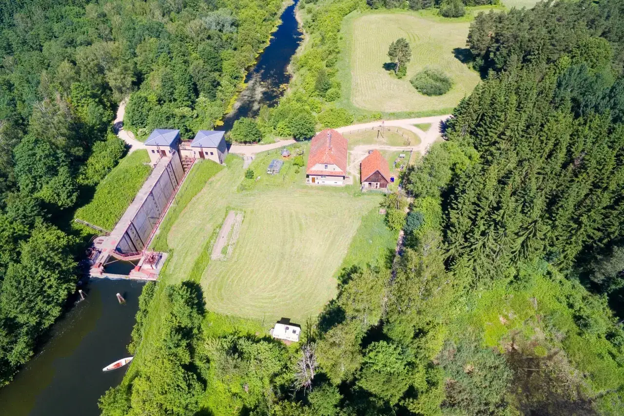 Widok z lotu ptaka na śluzę Leśniewo Górne, otoczoną zielenią. Widać kanał, budynki i fragment lasu.
