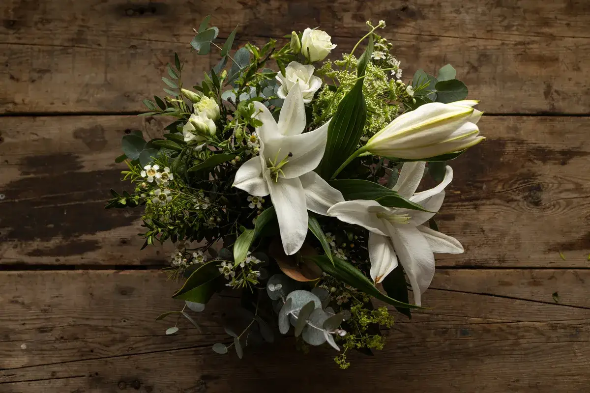Un ramo de novia con lirios blancos y rosas sobre madera r&uacute;stica. Un recuerdo para secar y atesorar.