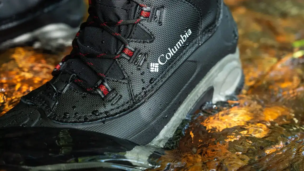 Columbia boots, designed to keep feet warm and dry, are submerged in shallow, clear water with golden reflections.
