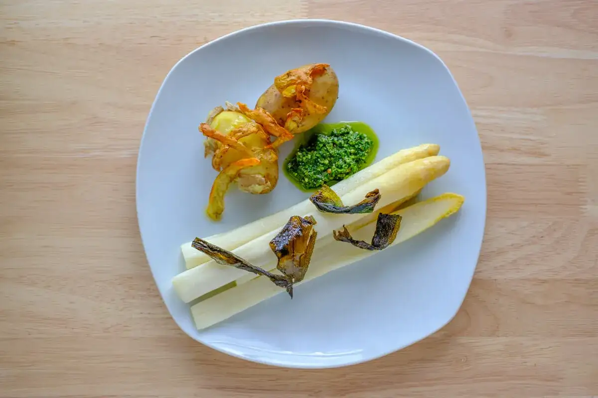 Ein Teller mit wei&szlig;em Spargel, der sous vide gegart wurde, dazu eine kleine Kartoffel mit knusprigen Schalen und gr&uuml;ner Sauce.