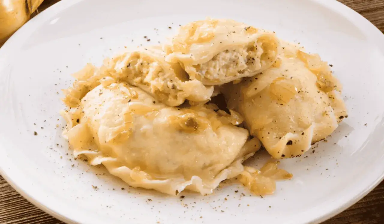 Pierogi ruskie z twarogiem i ziemniakami, polane skarmelizowaną cebulką i posypane pieprzem. Pyszne i sycące danie.