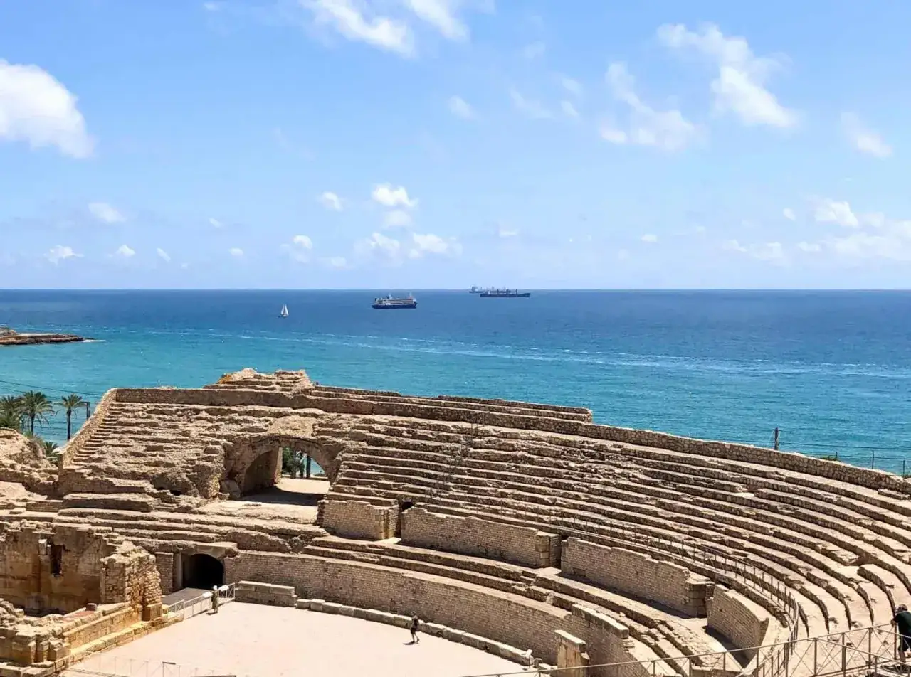 Ancient Roman amphitheater overlooking the Mediterranean Sea, a must-see for Tarragona things to do. Ships sail on the blue water under a cloudy sky.