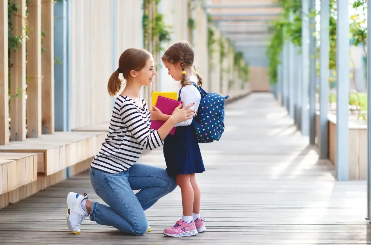 Mama wspiera córkę z dysleksją przed szkołą. Dziecko z plecakiem i książkami czuje się niepewnie, ale mama dodaje mu otuchy.
