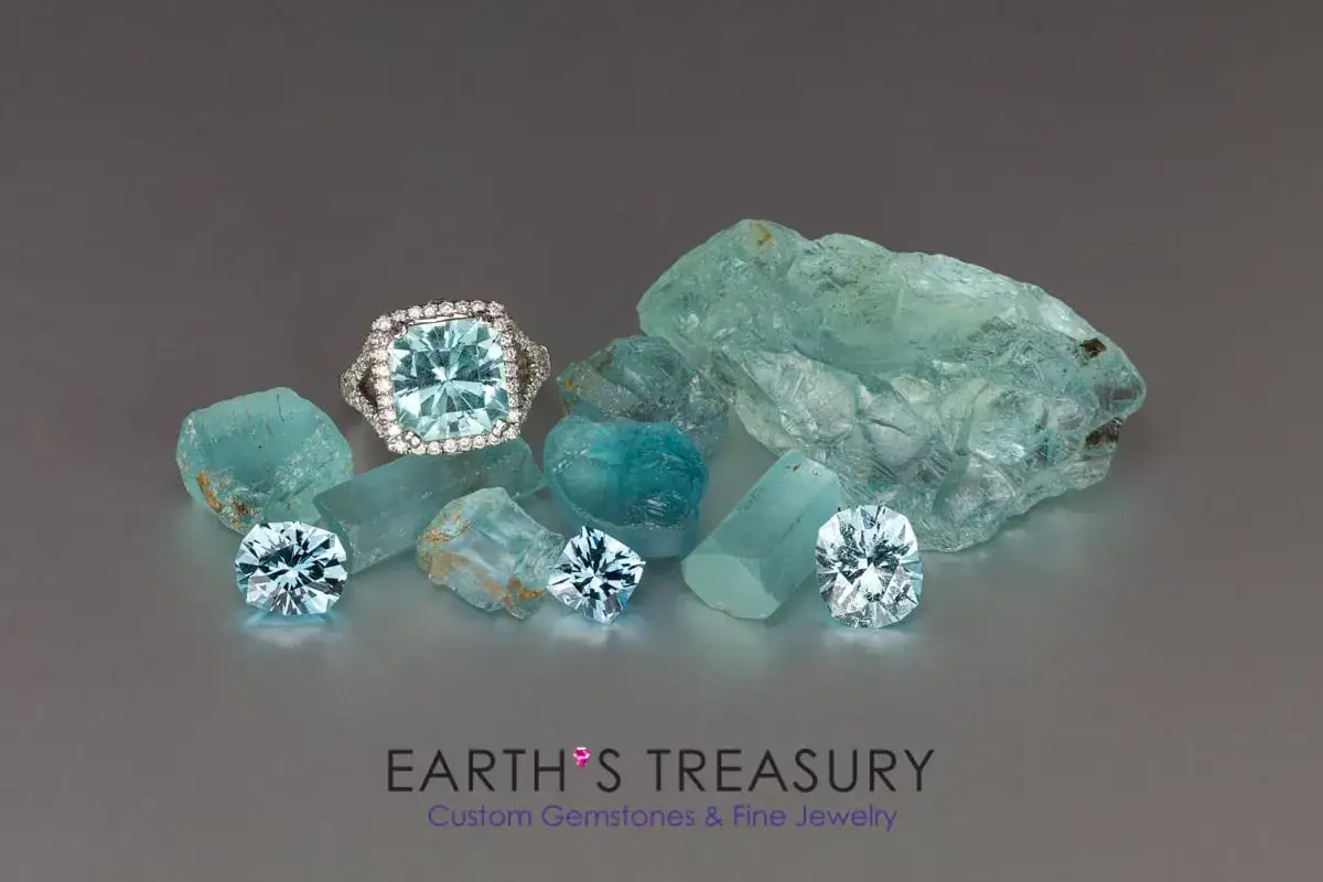 Anello con acquamarina pietra centrale circondato da diamanti, su un letto di acquamarine grezze e tagliate.