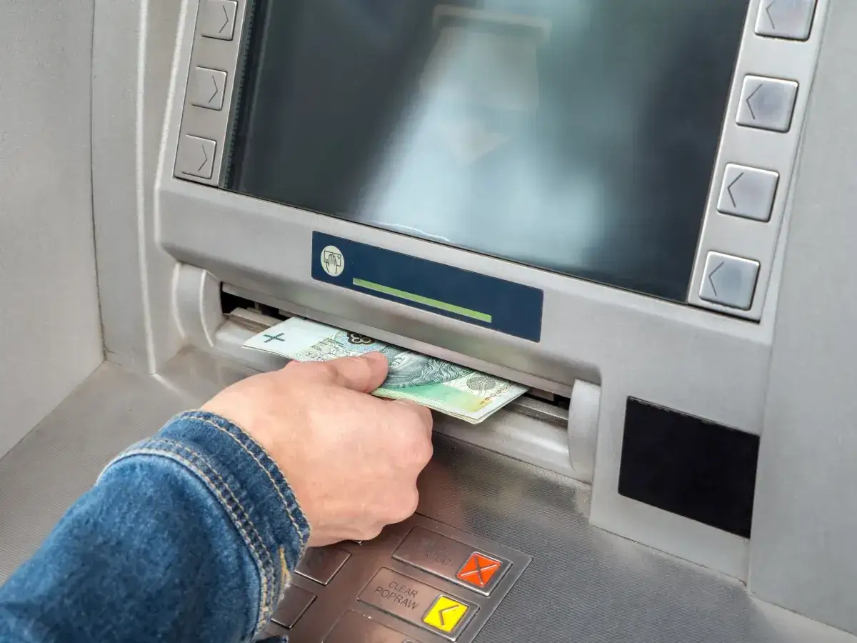 Ręka wyciąga banknot z bankomatu. Czy Vivus wyplaca w sobote? Sprawdzam stan konta.