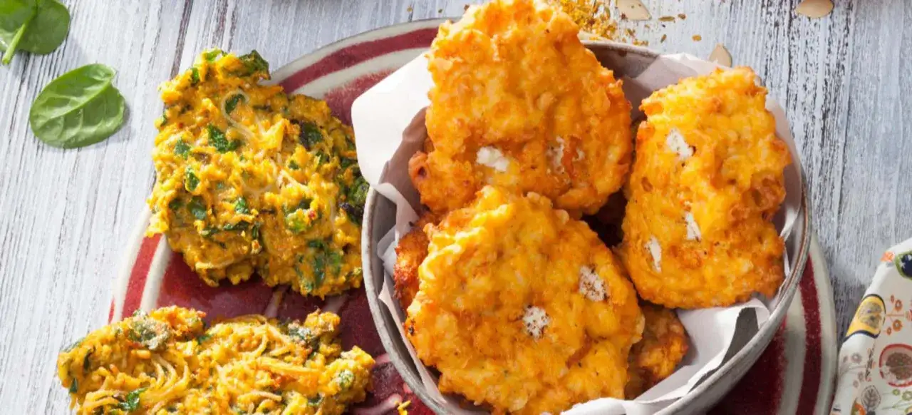 Buñuelos de espinacas dorados y crujientes, algunos con trozos de queso blanco, servidos en un plato y un cuenco.