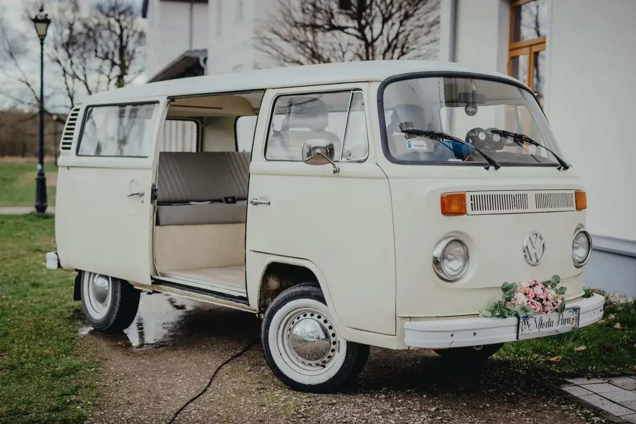 Kremowy VW T2 z otwartymi drzwiami, ozdobiony bukietem kwiatów i tabliczką