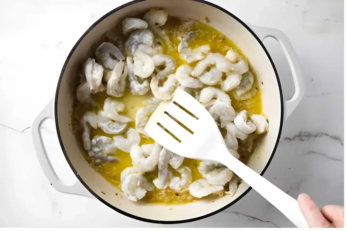 Crevettes crues dans une po&ecirc;le avec du beurre fondu, pr&ecirc;tes pour des p&acirc;tes aux crevettes. Une spatule blanche remue le tout.