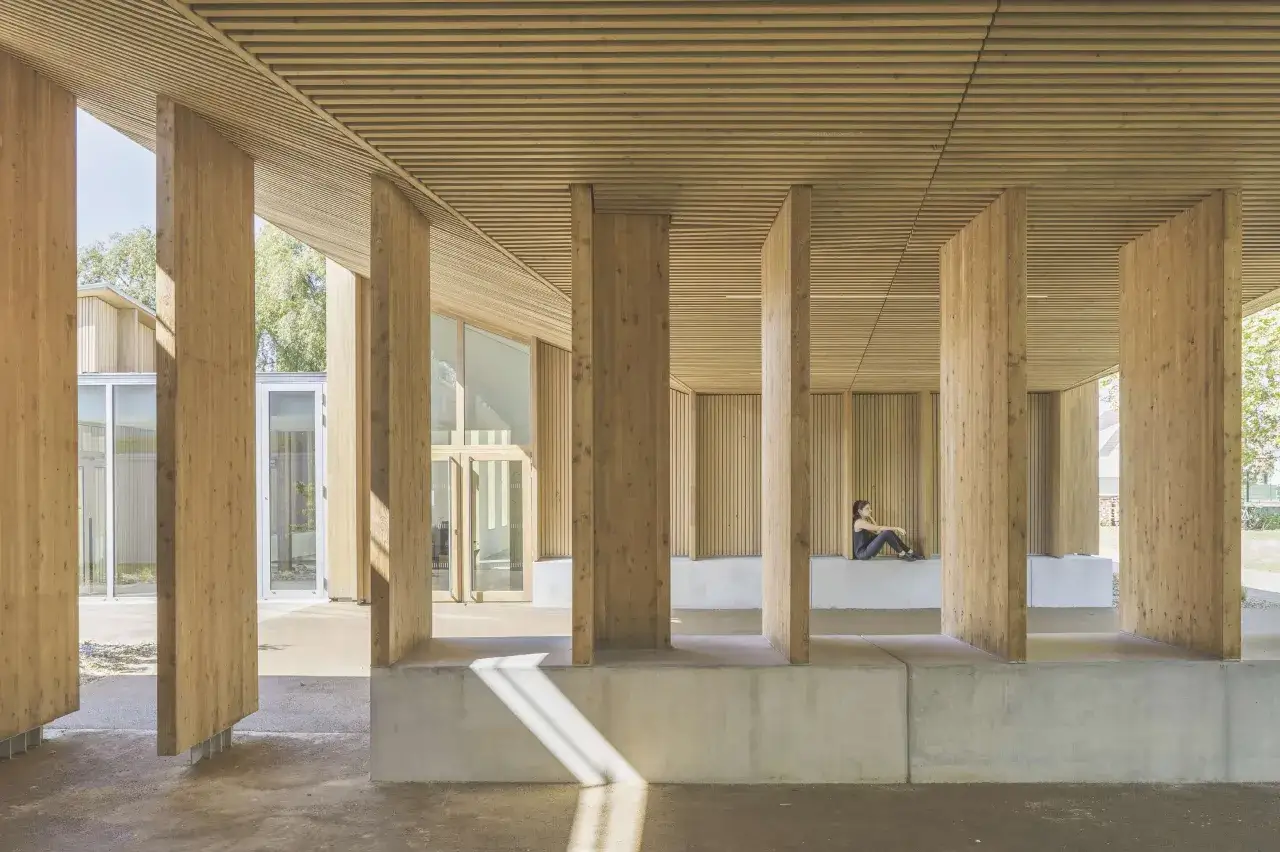 Une personne assise sous une impressionnante structure bois, avec des piliers massifs et un plafond lamell&eacute;.