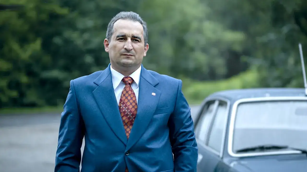 Michał Koterski w garniturze, obok starego samochodu, jak z jego filmów.