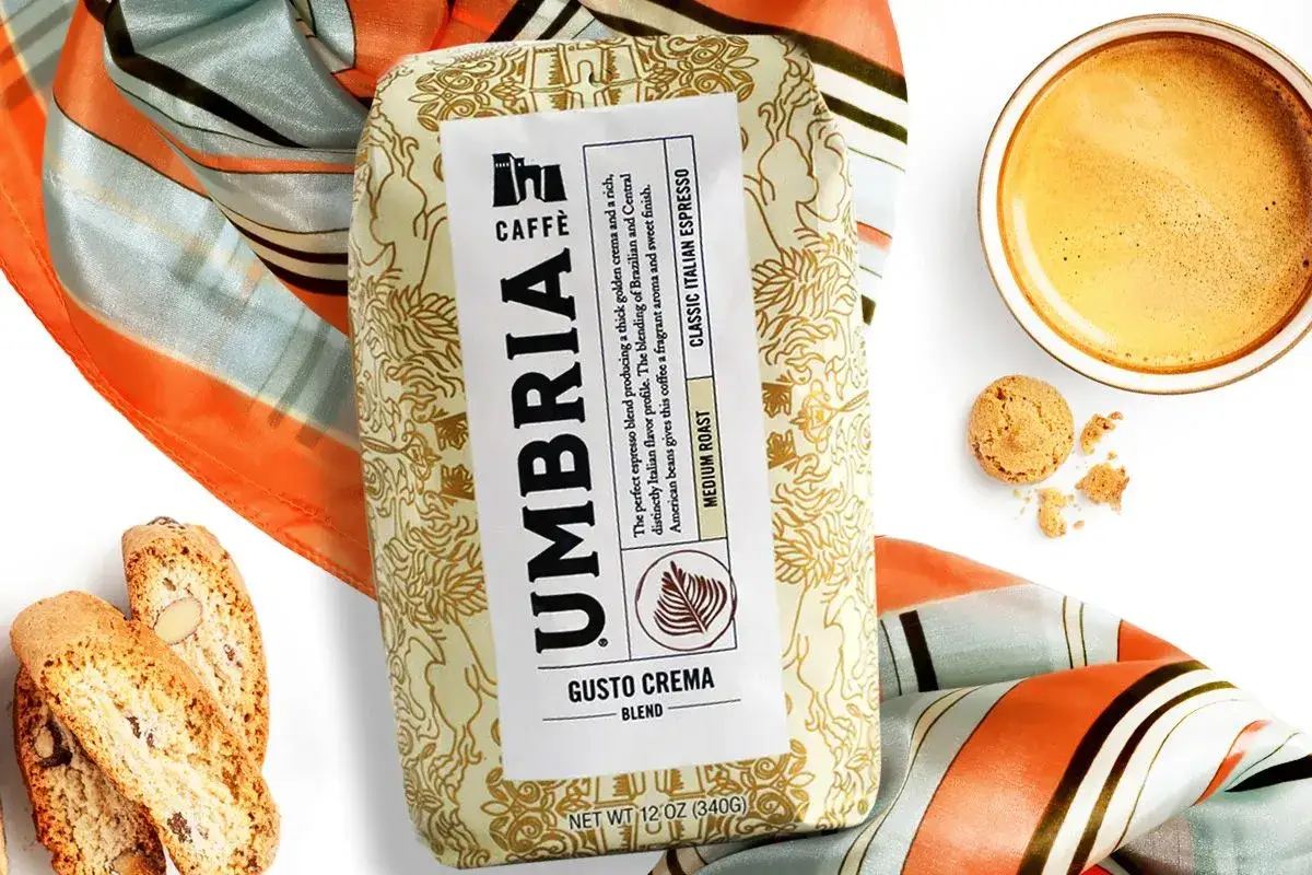 Kawa do ekspresu Umbria Gusto Crema, idealna do włoskiego espresso. Obok filiżanka kawy, biszkopty i chusta.