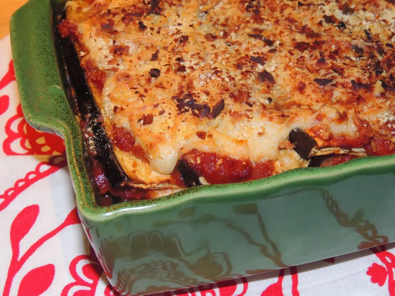 Un plat de moussaka végétarienne gratinée, avec des couches d'aubergines, de sauce tomate et de béchamel, dans un plat vert.