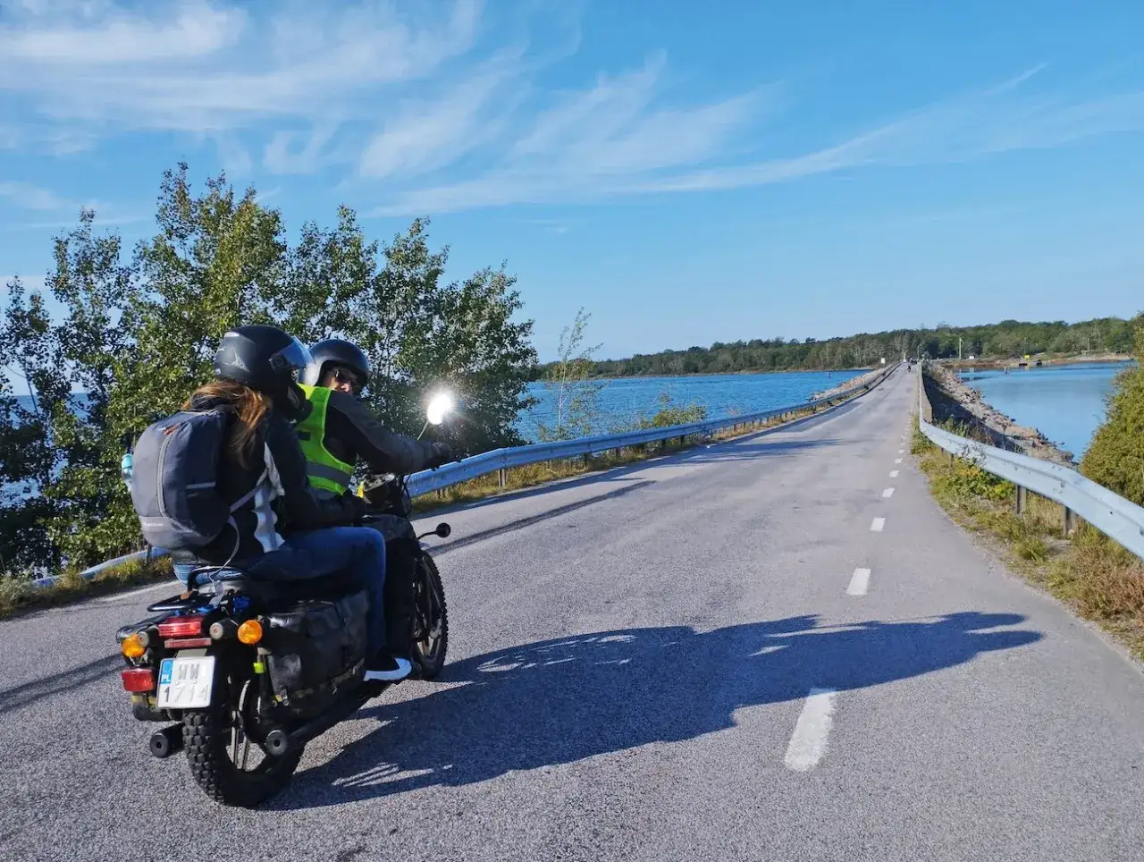 Para podróżuje motocyklem przez malowniczą Szwecję, pokonując most nad spokojną wodą.