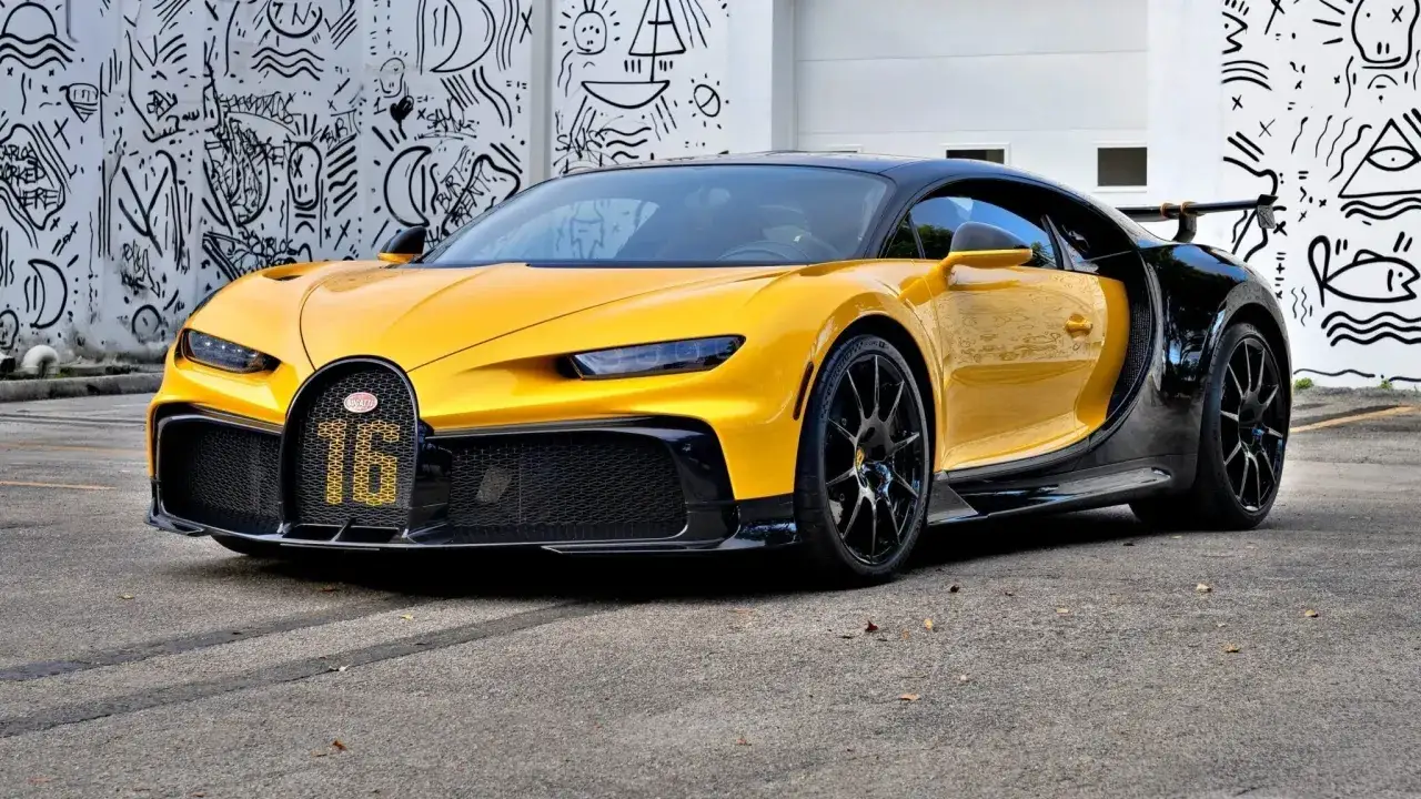Żółto-czarny Bugatti Chiron, którego cena jest astronomiczna, zaparkowany przed ścianą z czarno-białymi rysunkami.