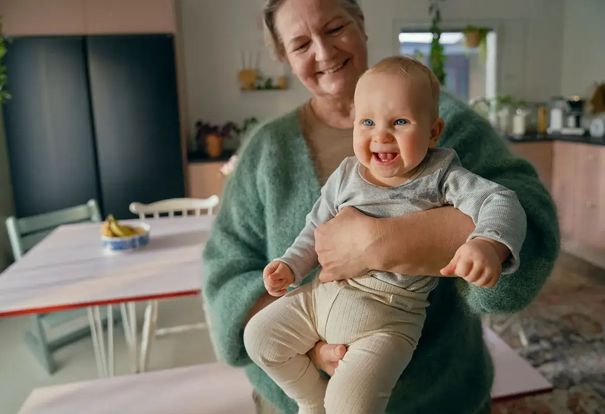 Glad farmor h&aring;ller sitt barnbarn f&ouml;r 10 m&aring;naders kontroll p&aring; BVC. Barnet ler stort med bl&aring; &ouml;gon.