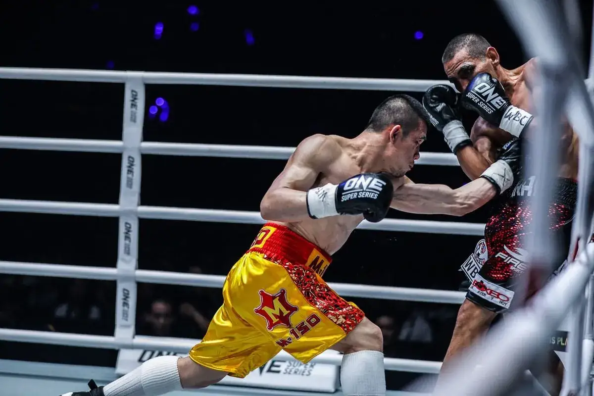 Boxer in yellow shorts throws a shovel hook as his opponent prepares an uppercut in a fierce ONE Championship bout.