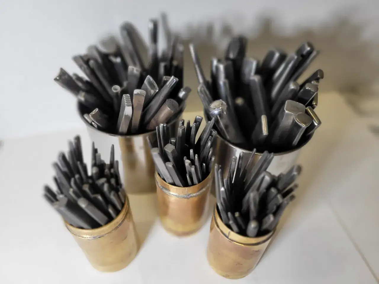 Ensemble d'outils de **orfèvre** dans des pots en métal et en laiton, prêts à façonner le métal précieux.