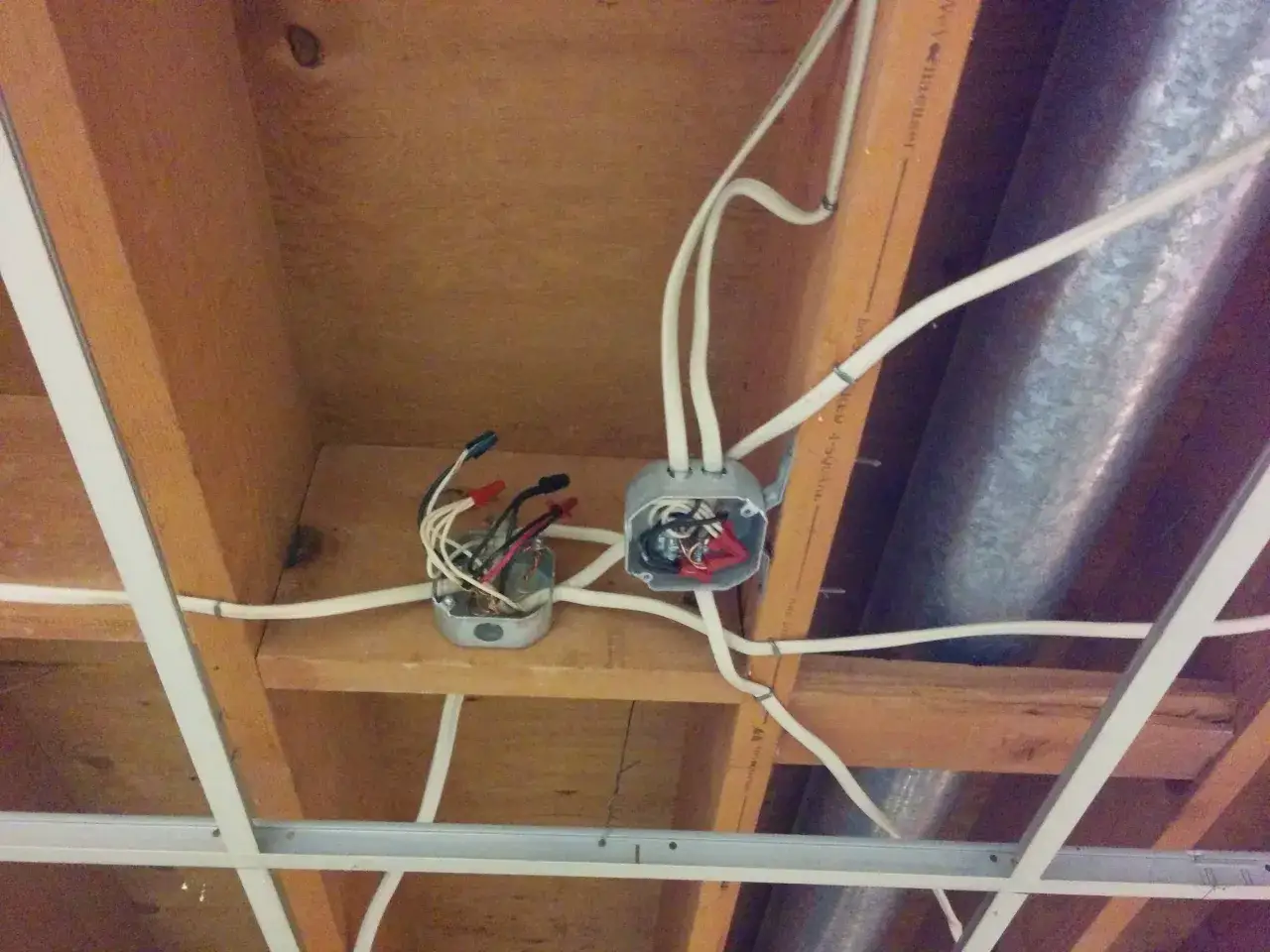 Instalación eléctrica en techo de madera, con cajas de registro y cables. Se observa cómo se busca sacar un punto de luz de otro existente.