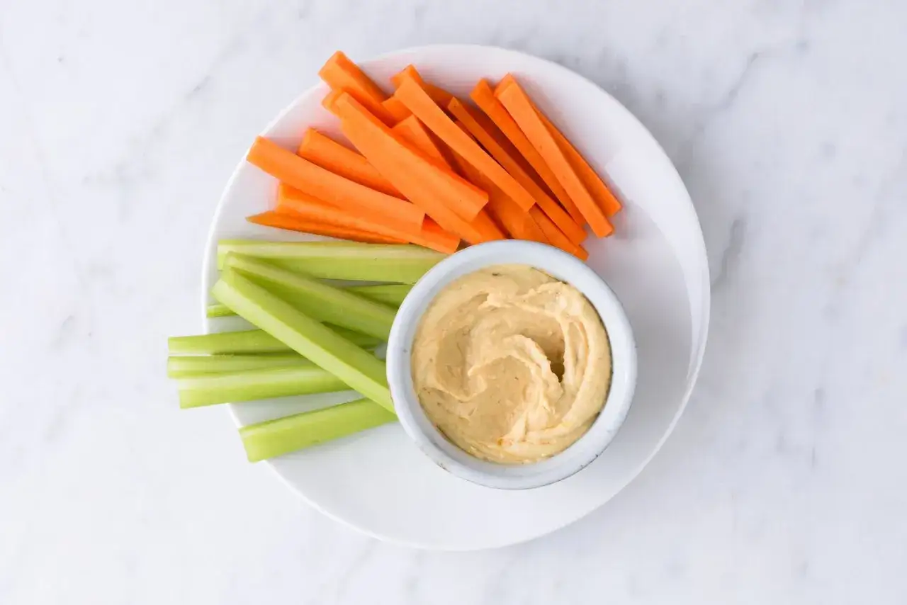 Geschnittene Karotten- und Selleriestifte mit Hummus. Ein gesunder Snack, der wenig Hummus-Kalorien hat.