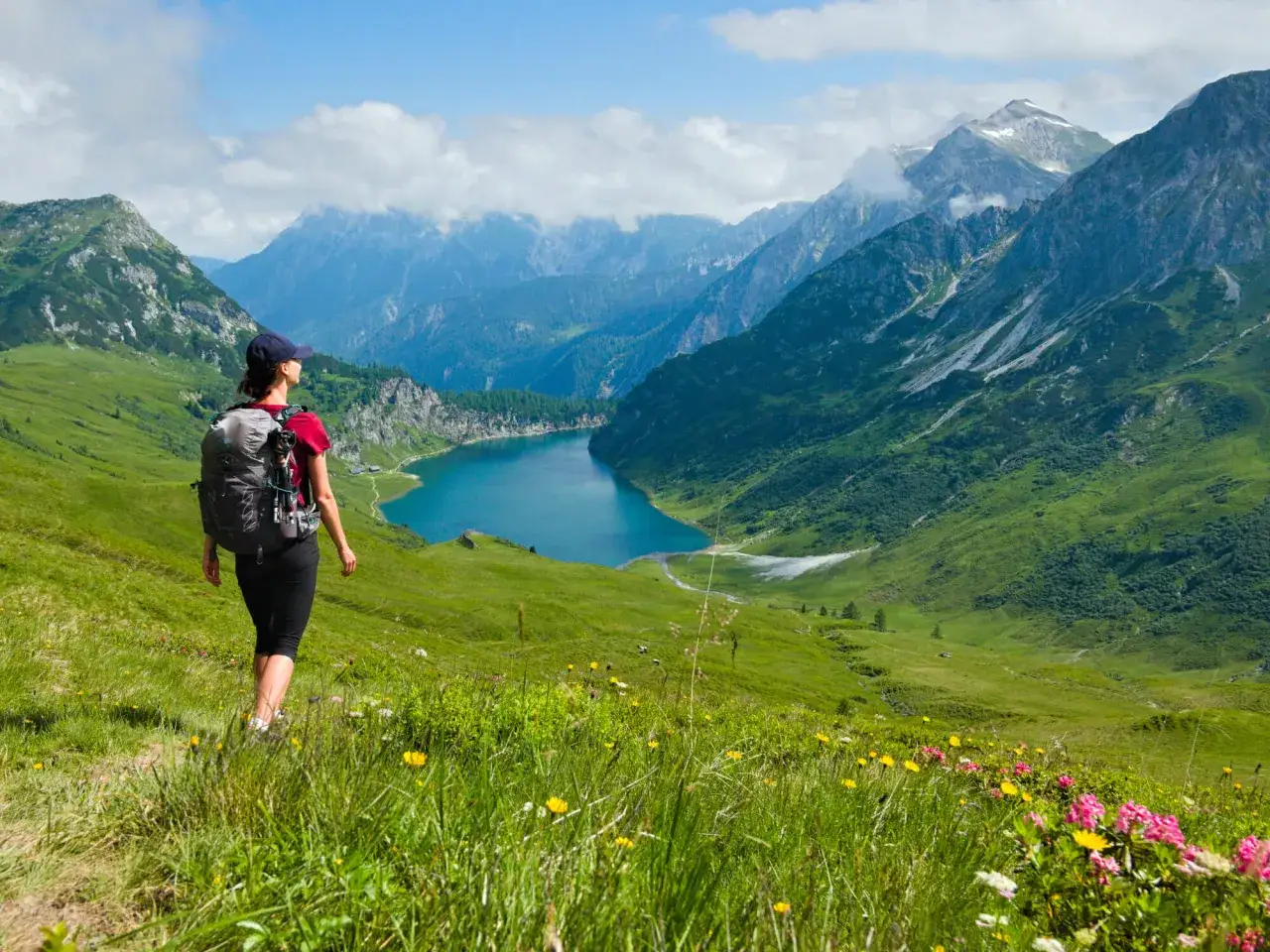 Wanderin mit Rucksack genießt den atemberaubenden Ausblick auf einen Bergsee. Perfekter sommerurlaub in Bayern.