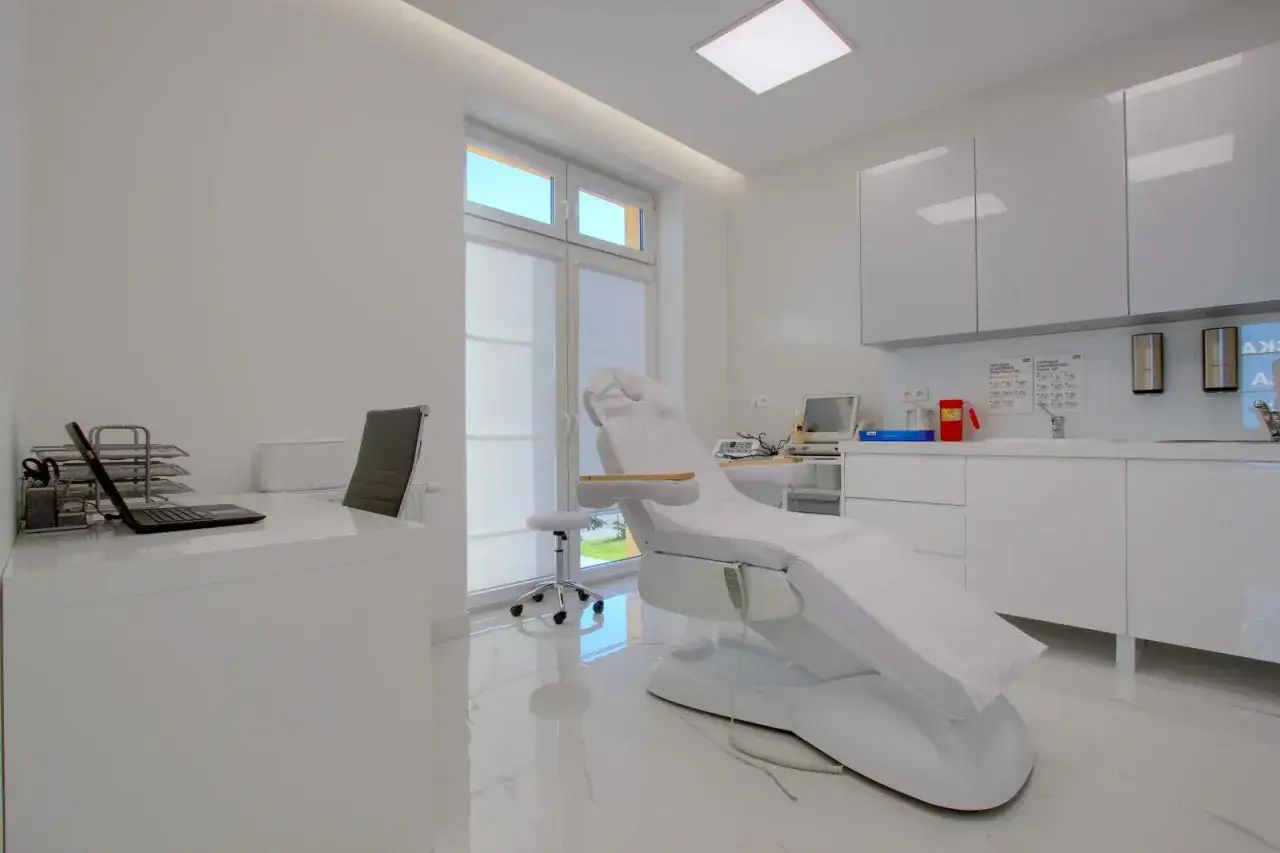 Nowoczesny gabinet dermatologiczny z fotelem zabiegowym, biurkiem i szafkami.