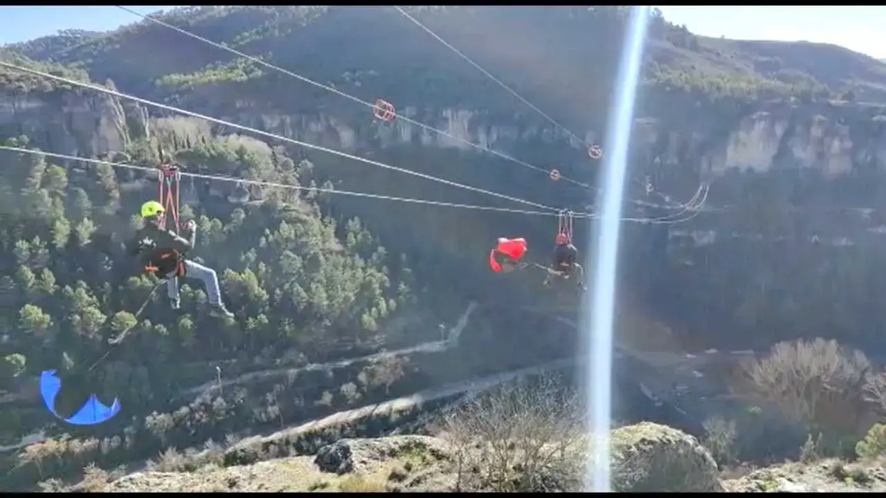 Dos personas disfrutan de la tirolina de Cuenca, cruzando un ca&ntilde;&oacute;n con vistas a un bosque y monta&ntilde;as.