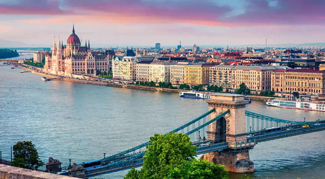 Iconic Chain Bridge spans the Danube, with the Hungarian Parliament Building and cityscape visible. A perfect view for your Budapest travel guide.