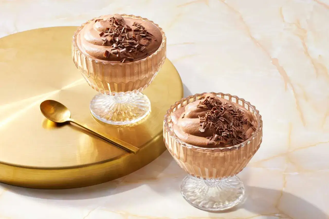 Tv&aring; glas med kr&auml;mig chokladmousse, toppad med chokladsp&aring;n. Perfekt f&ouml;r ett enkelt chokladmousse recept. En guldig sked ligger bredvid.