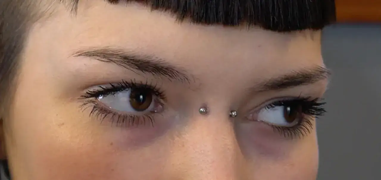 Zbliżenie na twarz z widocznym bridge piercingiem między brwiami.