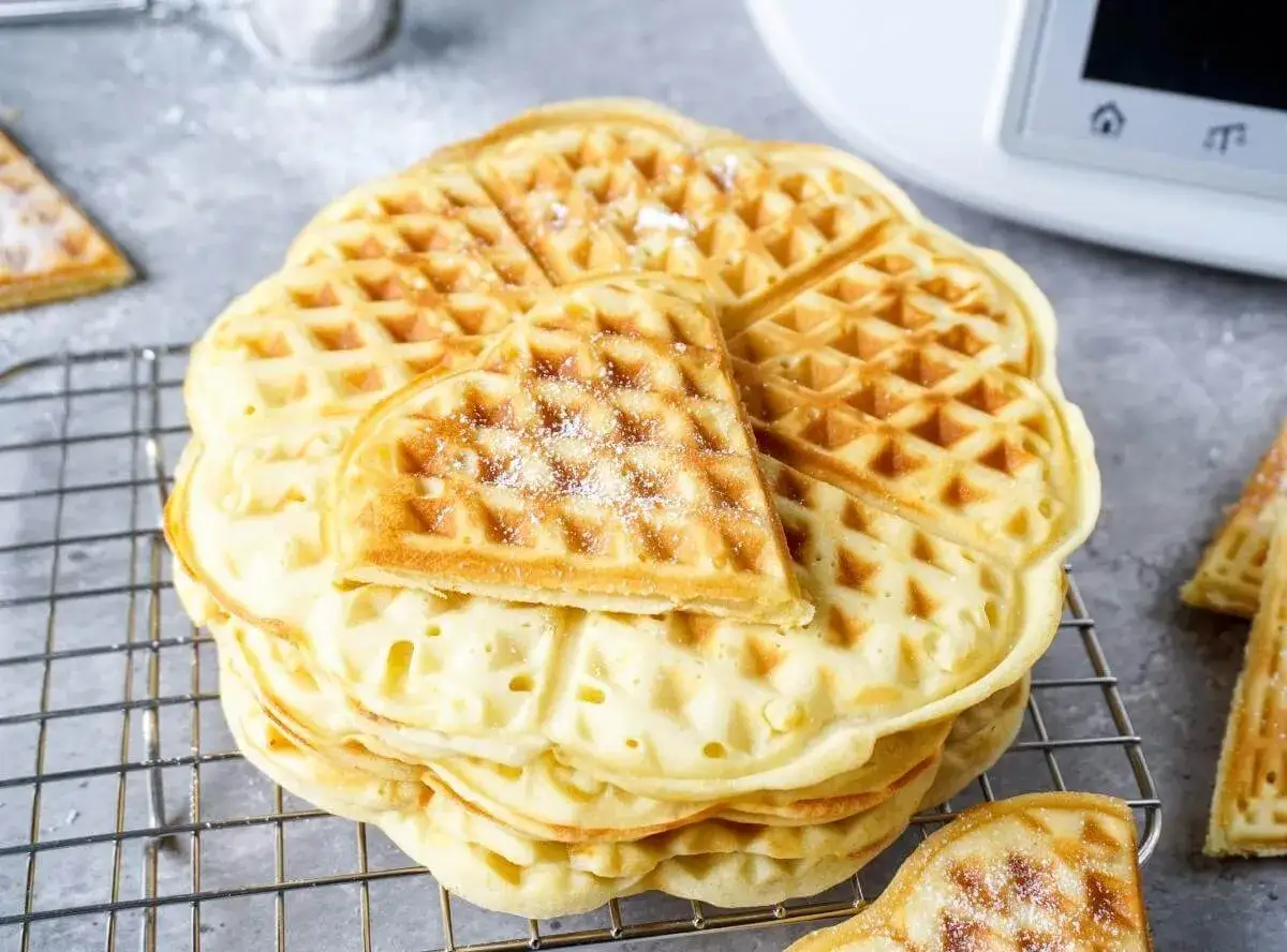 Goldbraune, fluffige Waffeln, frisch aus dem Thermomix, auf einem Gitterrost, mit Puderzucker best&auml;ubt.