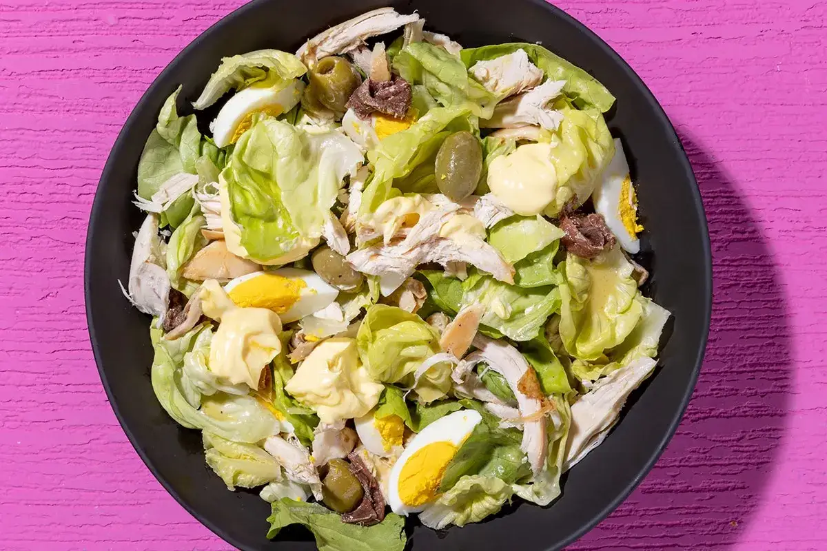 Insalata di pollo sfiziosa con uova sode, olive verdi, acciughe e maionese su letto di lattuga croccante.