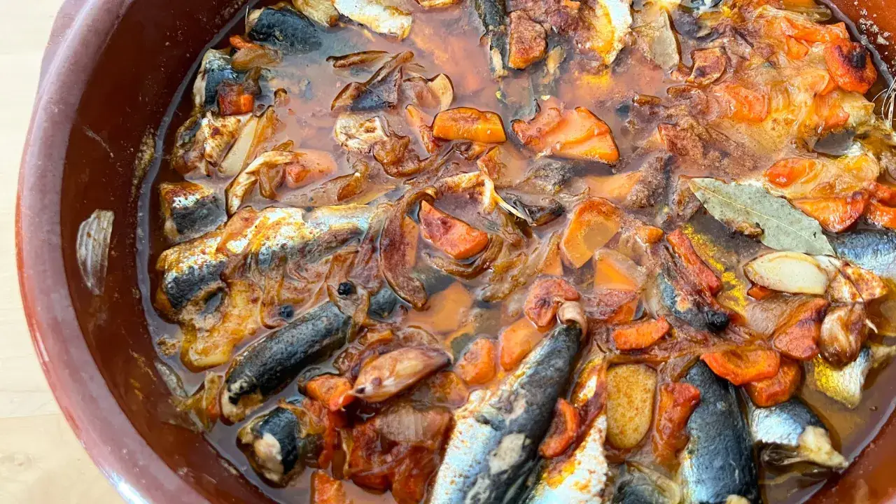 Sardinas en escabeche cocinándose en una cazuela de barro con verduras.