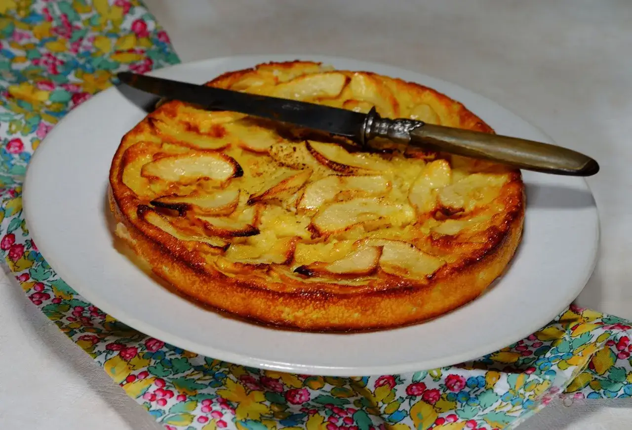 Gâteau aux pommes doré, une recette facile et originale. Un couteau repose sur ce délice fruité, prêt à être dégusté.