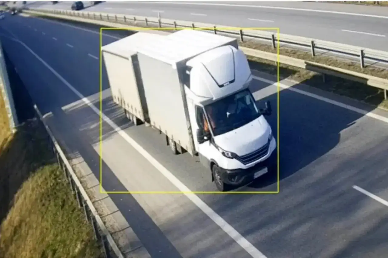 Biała ciężarówka z naczepą jedzie autostradą. System viatoll monitoruje ruch pojazdów.