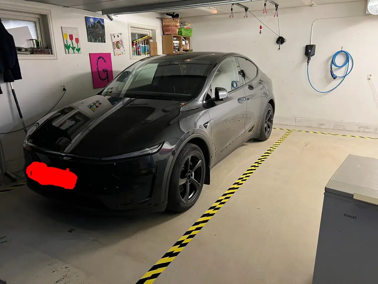 Czarny Tesla Y w garażu, obok ładowarki. Wymiary tego SUV-a pozwalają na komfortowe parkowanie.