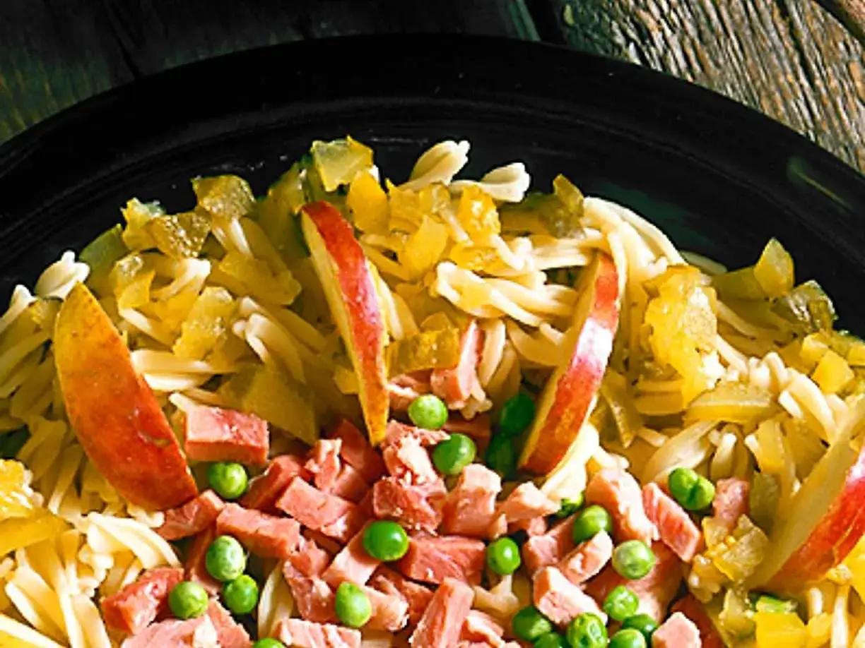 En n&auml;rbild p&aring; en l&auml;cker pastasallad med skinka, &auml;ppelklyftor och gr&ouml;na &auml;rtor.
