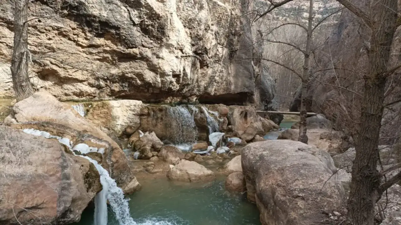Cascada y río en un cañón rocoso, con un puente de madera y vegetación invernal. Las pasarelas de Valloré invitan a explorar este paisaje.