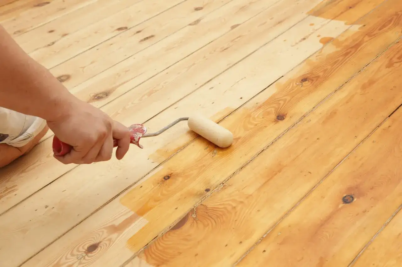 Hand versiegelt Parkett mit einer Rolle. Der Boden wird gleichm&auml;&szlig;ig mit einer sch&uuml;tzenden Schicht &uuml;berzogen, um ihn haltbarer zu machen.