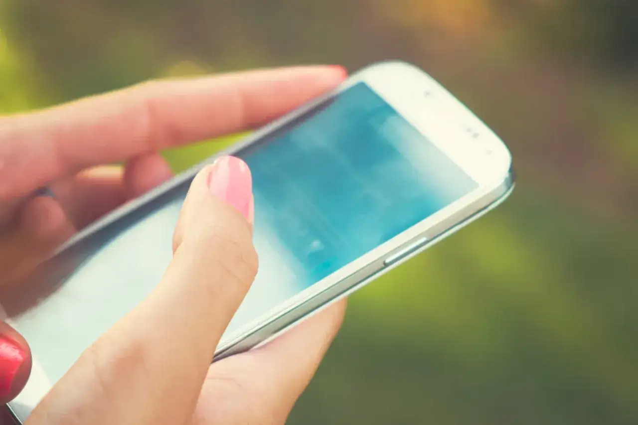 Dłonie trzymające smartfon, sprawdzające, co to roaming, by nie przepłacić za połączenia za granicą.