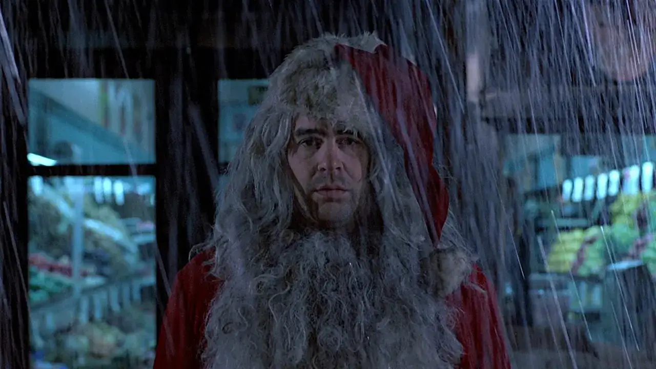 Un Babbo Natale con barba e cappello, sotto la pioggia, ricorda la scena di