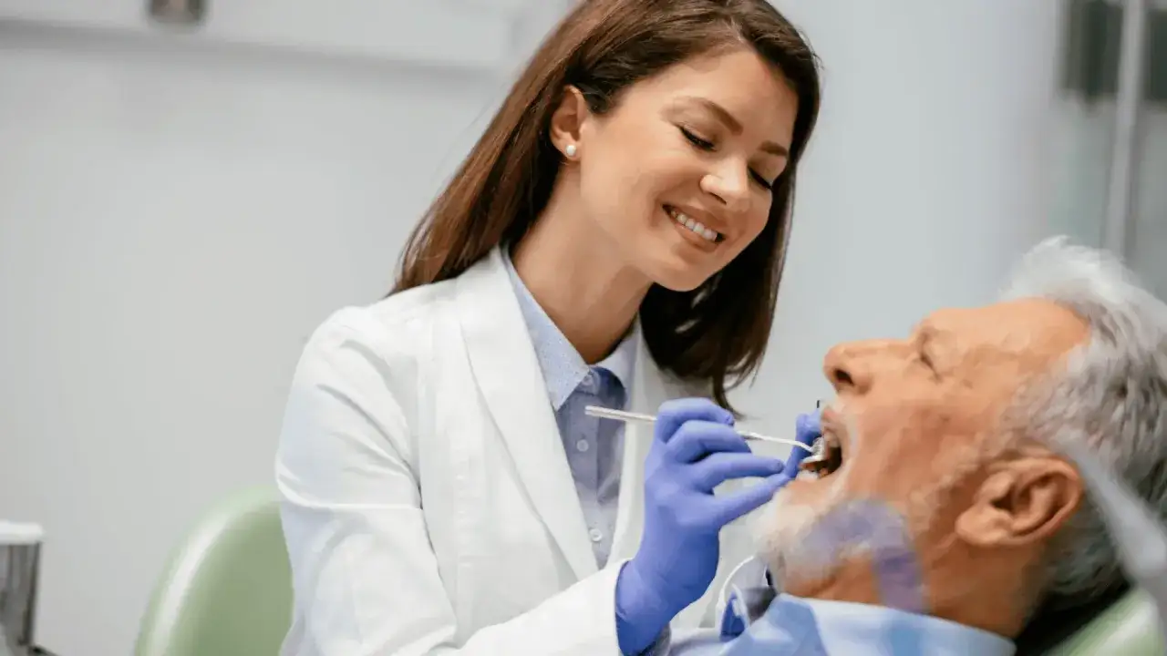 Uśmiechnięta dentystka wykonuje zabieg endodoncji u starszego mężczyzny. To leczenie kanałowe, które ratuje zęby.