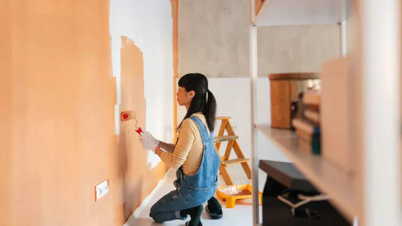 Frau malt Wand in Orange. Sie fragt sich, wie lange braucht wandfarbe zum trocknen, w&auml;hrend sie die Farbe auftr&auml;gt.