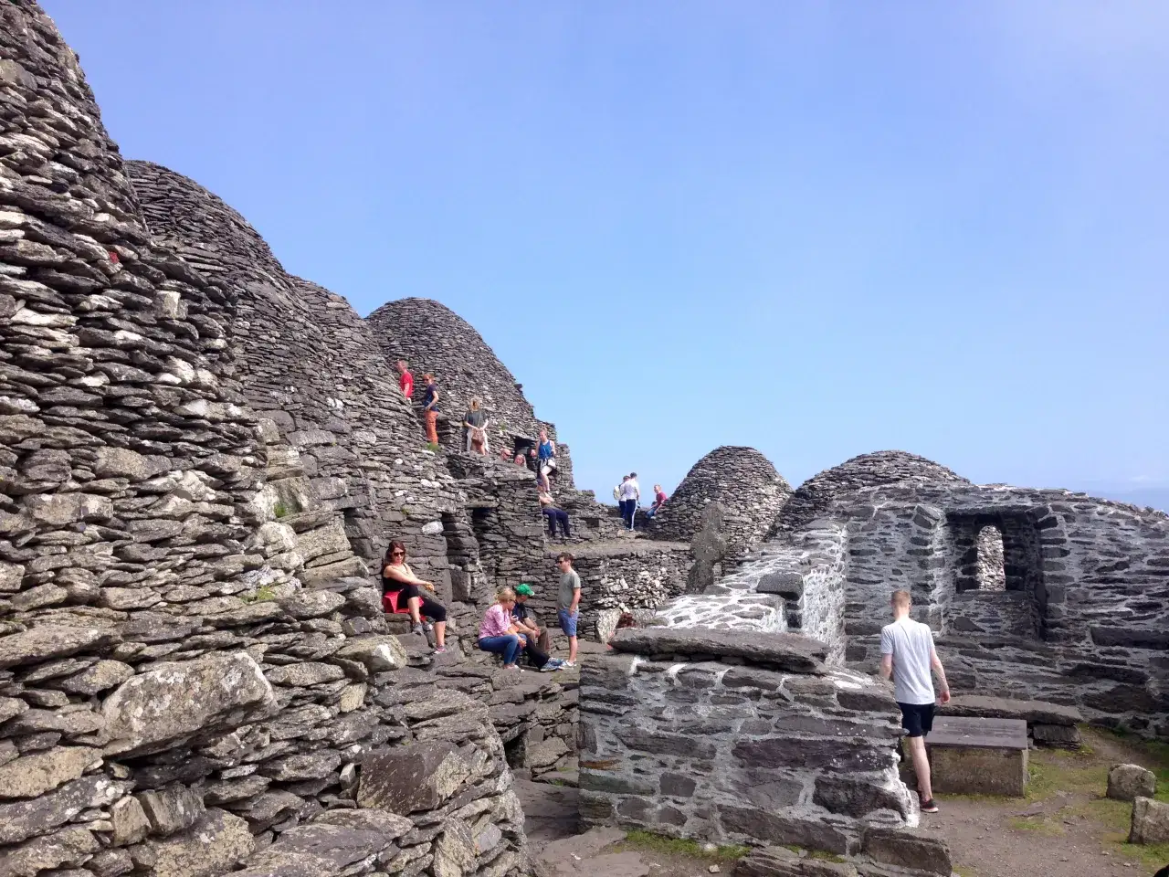 Turyści zwiedzają kamienne ruiny na Skellig Michael. Planując logistykę trasy, warto uwzględnić trudne podejście i ograniczoną liczbę miejsc.
