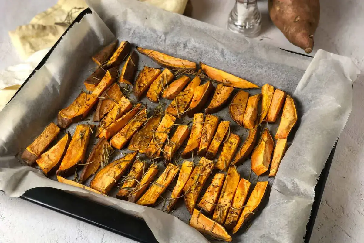Patate dolci al forno, tagliate a spicchi e condite con rosmarino, pronte per essere gustate.