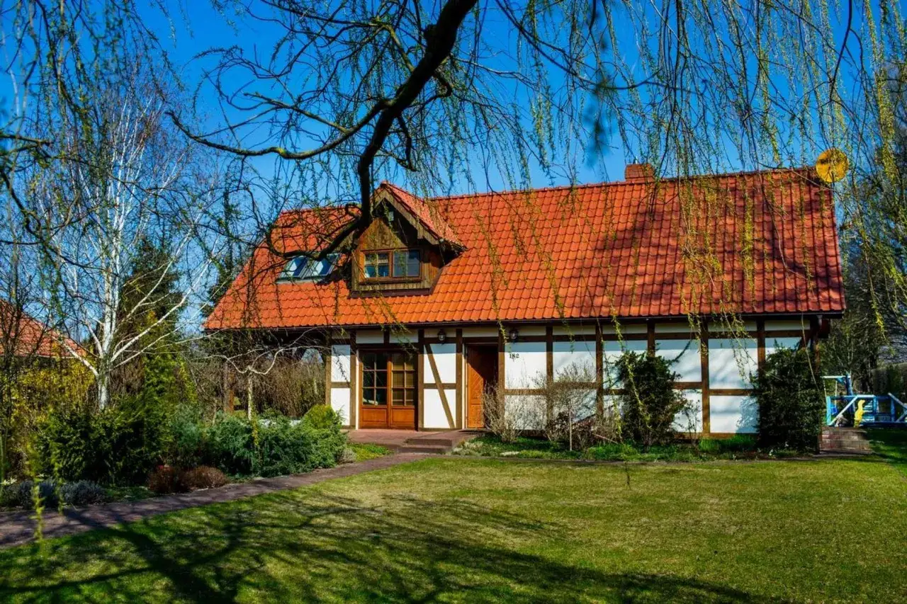 Urokliwy dom z czerwonym dachem, otoczony zielenią. Idealne miejsce na agroturystykę nad morzem.