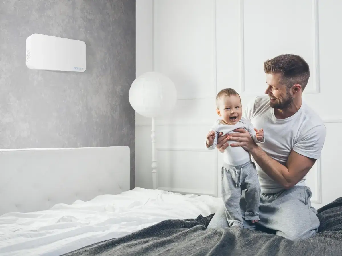Padre gioca con il suo bambino su un letto. Sopra il letto, un dispositivo VMC come funziona per garantire aria pulita.